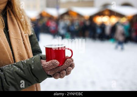 Frau mit rotem Becher mit Glühwein oder Punsch aus heißen Getränken auf dem traditionellen Weihnachtsmarkt. Genuss des Adventurlaubs in der Stadt Stockfoto