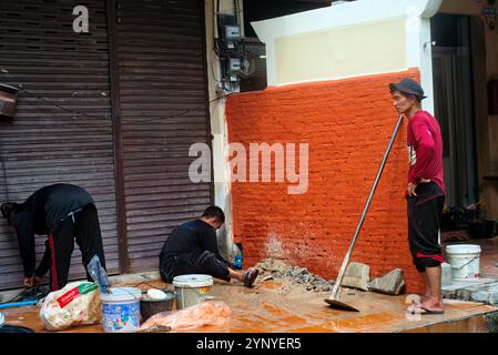 Pattaya, Thailand - 9. Oktober 2024: Drei thailändische Männer in der Innenstadt renovierten ein geschlossenes Geschäft in der Nähe einer kleinen, orangen Mauer. Stockfoto