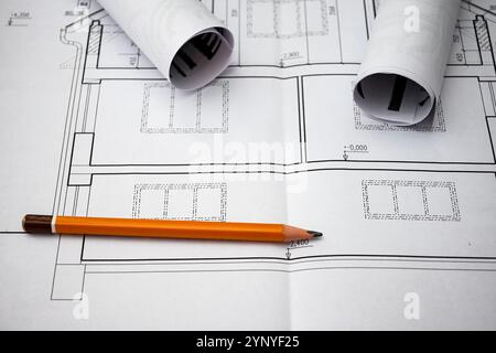 Architekturzeichnungen mit Hausplänen, begleitet von einem Bleistift und aufgerollten Bauplänen, die den Entwurfs- und Bauprozess symbolisieren. Stockfoto