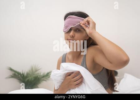 In der Nahaufnahme erhebt sich die Frau in Schlafmaske widerwillig, hegt Alarm, verfolgt von Schlaflosigkeit. Stockfoto