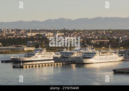 Dockingboote mit weißen und blauen Jadrolinija Juraj Dalmatinac, Jadran Rijeka und Ugljan Rijeka Fähren im Hafen von Zadar mit Skyline und Bergkette in BA Stockfoto