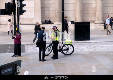 Ein Metropolitan Police Community Support Officer, der einem Mitglied des öffentlichen Mannes mit einem Mobiltelefon bei Wegbeschreibungen hilft City of London UK 2024 Stockfoto