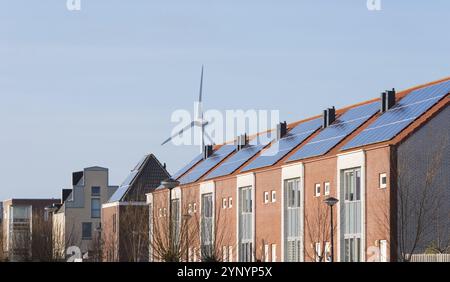 Reihenhäuser mit Solarpaneelen vor einer großen Windmühle Stockfoto