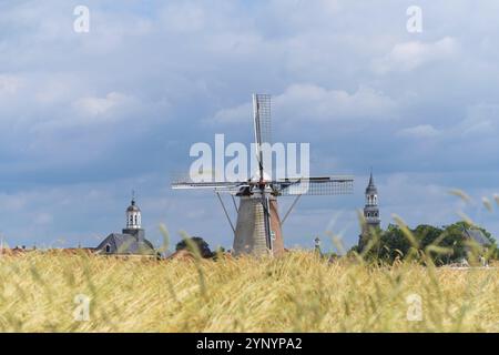 Feld mit reifem Weizen vor einem kleinen Dorf mit einer Windmühle und mehreren Kirchtürmen Stockfoto