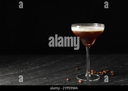 Ein Glas köstlicher Espresso-Martini und Kaffeebohnen auf einem dunklen, strukturierten Tisch. Leerzeichen für Text Stockfoto