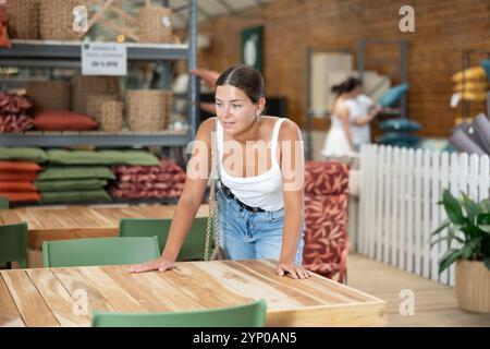 Positives Mädchen wählt sorgfältig einen Holztisch für ein Landhaus im Gartengeschäft Stockfoto