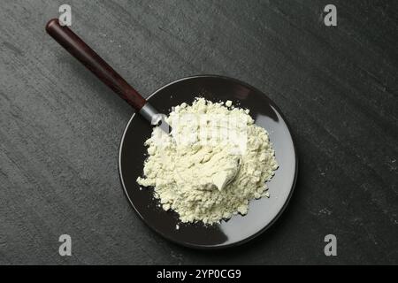 Teller mit trockenem Wasabi-Pulver und Löffel auf dunkel strukturiertem Tisch, Draufsicht Stockfoto