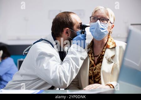 Männlicher Arzt führt eine Ohruntersuchung an älteren Frauen mit Otoskop bei Arztterminen sorgfältig durch. Arzt mit diagnostischem Hilfsmittel bei Rentnerinnen während des Hörtests in der Klinik. Stockfoto