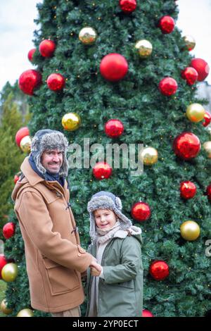 24. November 2024: Vater und Sohn vor einem prachtvoll geschmückten Weihnachtsbaum mit bunten Weihnachtskugeln in der Stadt - ein warmer Moment einer Familie zur Weihnachtszeit, ein Symbol voller Freude und winterlicher Geist. *** Vater und Sohn vor einem prachtvoll geschmückten Weihnachtsbaum mit bunten Weihnachtskugeln in der Stadt ein herzlicher Moment einer Familie in der Weihnachtszeit, Symbol voller Freude und winterlicher Festtagsstimmung. Stockfoto