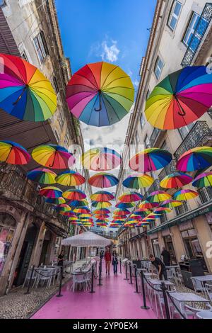 Lissabon, Portugal. 13. November 2023: Rosa Straße (Rua Nova do Carvalho) mit farbenfrohen Regenbogenschirmen, die zwischen Gebäuden hängen Stockfoto