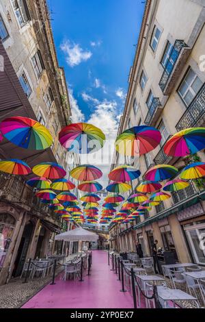 Lissabon, Portugal. 13. November 2023: Rosa Straße (Rua Nova do Carvalho) mit farbenfrohen Regenbogenschirmen, die zwischen Gebäuden hängen Stockfoto