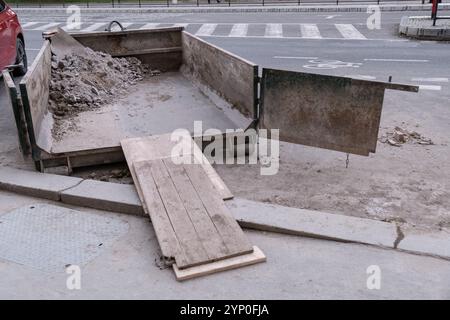 Ein offener Müllcontainer, der teilweise mit Bauabfällen gefüllt ist, wird auf einer Straße in der Stadt zur Entsorgung von Schutt abgestellt Stockfoto