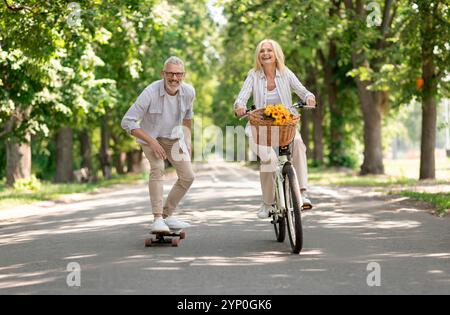 Moderne Rentner. Glückliches Seniorenpaar Mit Fahrrad Und Skateboard Im Park Stockfoto