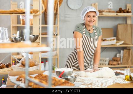 Frau arbeitet in der Bäckerei als Bäckerin, knetet Teig, arbeitet mit Mehl. Stockfoto