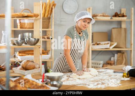 Frau arbeitet in der Bäckerei als Bäckerin, knetet Teig, arbeitet mit Mehl. Stockfoto