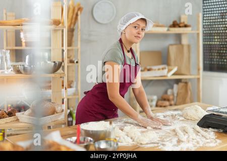 Mädchen arbeitet als Bäckerin in Bäckerei, formt Würstchen aus Teig, rollt lange runde Streifen aus Teig Stockfoto
