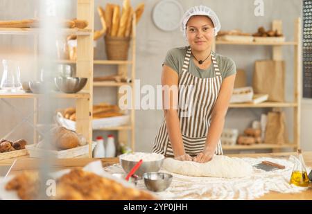 Frau arbeitet in der Bäckerei als Bäckerin, knetet Teig, arbeitet mit Mehl. Stockfoto
