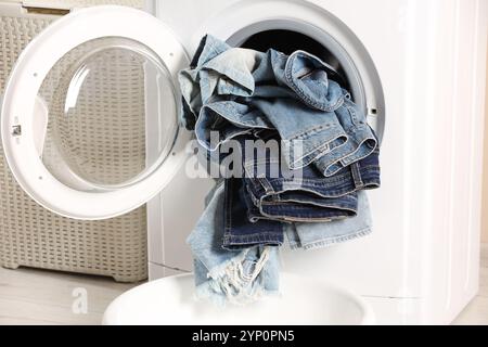 Waschmaschine mit schmutzigen Jeans und anderen Denim-Kleidern im Innenbereich Stockfoto