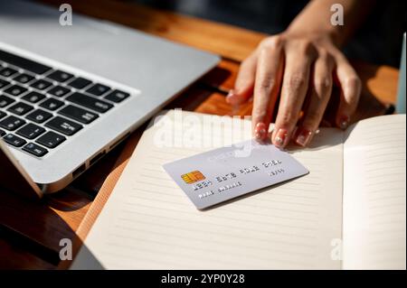Eine Nahaufnahme der Hand einer Frau, die eine Kreditkarte auf einem Tisch hält und Rechnungen online über ihren Laptop bezahlt. Finanzen, Investitionen, Online-Zahlungen, Online-Zahlungen Stockfoto