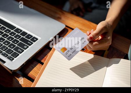 Eine Nahaufnahme der Hand einer Frau, die eine Kreditkarte auf einem Tisch hält und Rechnungen online über ihren Laptop bezahlt. Finanzen, Investitionen, Online-Zahlungen, Online-Zahlungen Stockfoto