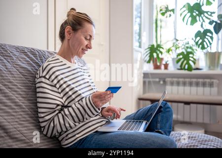 Glückliche Frau, die auf der Couch mit Laptop und Kreditkarte ruht. Online-Shopping im Internet, Lieferung nach Hause. Stockfoto