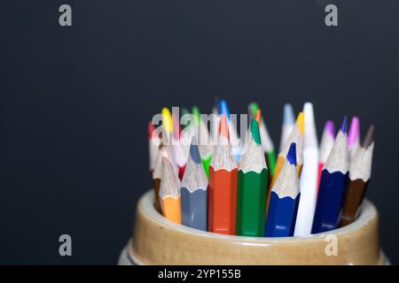 Hält Farbstifte in einem Keramikbecher mit schwarzem Hintergrund Stockfoto