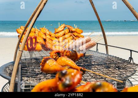 Hühnchen und Fisch werden gegrillt. Gebratene Hähnchenflügel auf einem Grill vor dem Hintergrund des Meeres und des Strandes mit weißem Sand Stockfoto