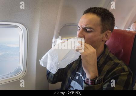 Übelkeit während des Fluges. Ein junger Kerl wird beim Transport krank. Junger Mann, der sich in der Papiertüte in der Flugzeugkabine erbricht. Konzept der Aerophobie und hoher PR Stockfoto