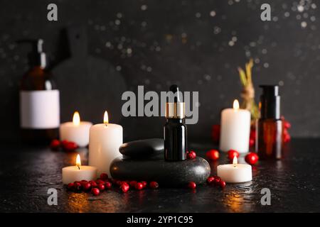 Komposition mit Flasche natürlichem ätherischem Öl, Spa-Steinen, brennenden Kerzen und Weißdorn auf dunklem Hintergrund Stockfoto