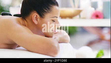 Glückliche Frau, entspannen oder massieren Sie im Spa mit heißen Steinen auf dem Rücken, um Verspannungen zu lösen, Stress zu lindern oder zu heilen. Weibliche Person, schlafend oder Klientin mit Stockfoto