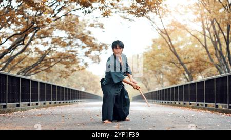 Kampfkunst, japanischer Mann und Holzschwert im Freien mit Kampf, Kampf und Samurai-Training auf der Straße. Park, Urban und Herausforderung mit Bambuswaffe, Kendo Stockfoto