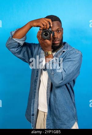 Junger Mann, der Fotos mit einer professionellen Kamera in einem Studio mit blauem Hintergrund macht Stockfoto