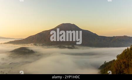 Ein ruhiger Morgen in den Bergen, wo sich Nebel um die Hügel schmiegt und das erste Licht des Tages einen goldenen Glanz über die Landschaft wirft. Stockfoto