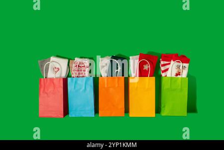 Farbenfrohe Papiertüten mit Weihnachtssocken auf grünem Hintergrund Stockfoto