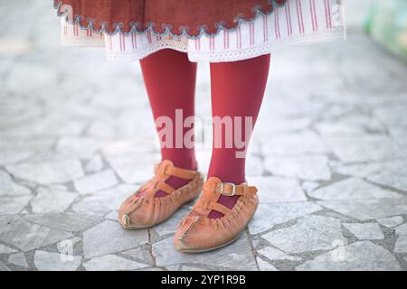 Echte traditionelle Tracht aus der Shope Region mit leuchtend roten Strümpfen, gesticktem Rock am Saum und unverwechselbaren Lederschuhen auf Kopfsteinpflaster. Stockfoto