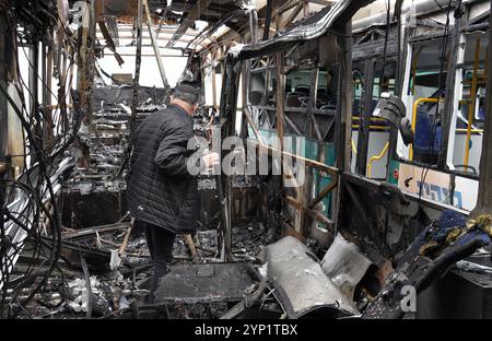 KIRYAT SHMONA, ISRAEL - 27. NOVEMBER: Ein Busfahrer inspiziert die Schäden in einem ausgebrannten Bus an der Stelle, an der ein Raketenangriff aus dem Libanon nur wenige Stunden vor dem Waffenstillstand zwischen Israel und Hisbollah in 2024 Kiryat Shmona nahe der Grenze zum Libanon über Nacht auf eine Bushaltestelle traf. Stockfoto