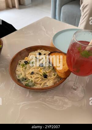 Spaghettischale mit Knoblauchbrot auf einem Tisch mit einem Glas Mojito. Stockfoto
