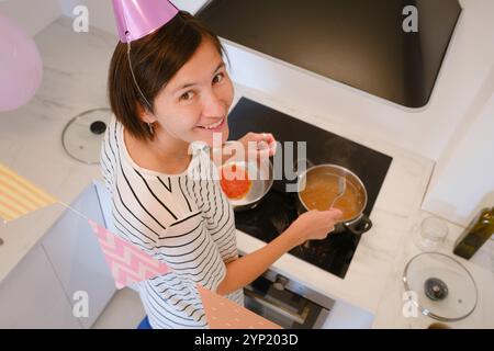 Die junge Frau feiert ihren Geburtstag zu Hause, umgeben von gemütlicher Atmosphäre und festlicher Dekoration. Sie kocht ein festliches Abendessen, leckere Pasta Stockfoto