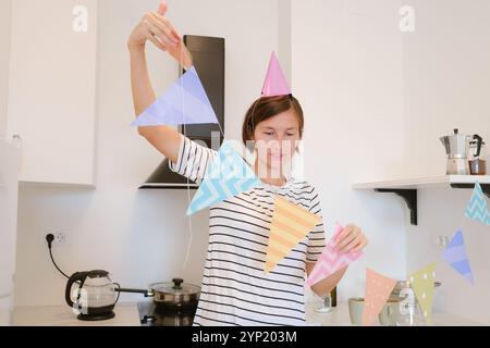 Die junge Frau feiert ihren Geburtstag zu Hause, umgeben von gemütlicher Atmosphäre und festlicher Dekoration. Sie genießt ihren besonderen Tag, bereitet sich auf den Urlaub vor, dekoriert die Küche Stockfoto