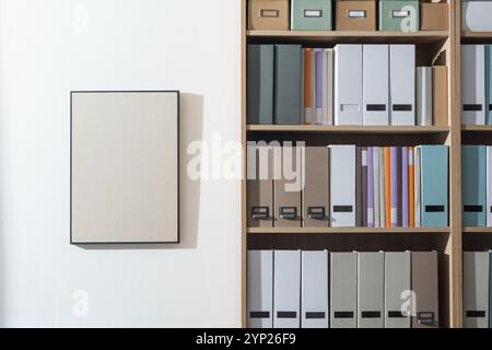 Aufgeräumtes Büro mit Ordnern und Büchern im Bücherregal, leeres Bild an der Wand, Aufbewahrungs- und Organisationskonzept Stockfoto