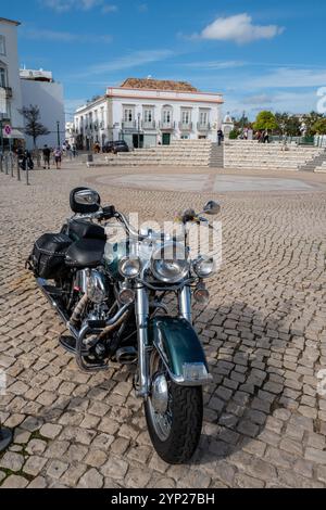 Harley Davidson Motorrad auf dem mit Kopfsteinpflaster gepflasterten Hauptplatz (Praca da República) von Tavira, einem beliebten Wintersonnenziel an der Algarve, Portugal Stockfoto