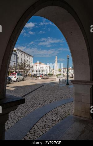 Der mit Kopfsteinpflaster gepflasterte Hauptplatz República von Tavira durch einen Bogen, Tavira, Algarve, Portugal Stockfoto