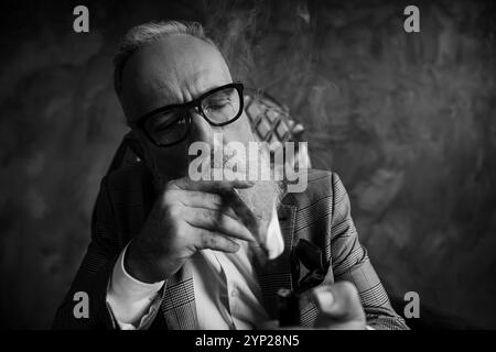 Nahaufnahme Porträt von attraktiv, ideal, atemberaubend, brutal, hart, Alter Mann, Dandy in Gläsern, Smoking auf Feuerzigarre auf grauem Hintergrund Stockfoto