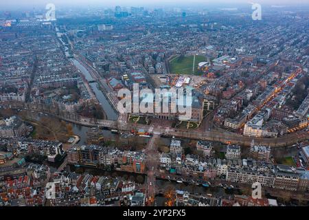 Blick aus der Vogelperspektive auf Amsterdams berühmtes Rijksmuseum, umgeben von historischen Kanälen, lebhaften Vierteln und einem leuchtenden abendlichen Stadtbild Stockfoto
