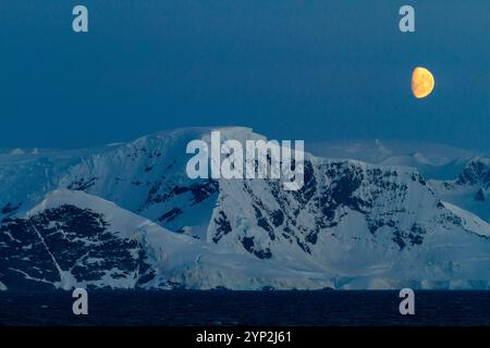 Blick auf den fast Vollmond, der über schneebedeckten Bergen auf der Antarktischen Halbinsel, Antarktis und Polarregionen aufsteigt Stockfoto