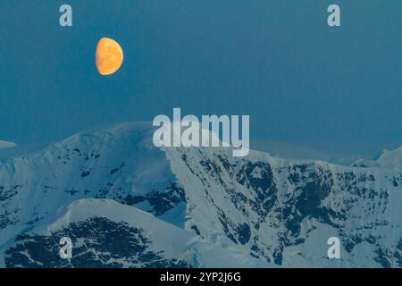 Blick auf den fast Vollmond, der über schneebedeckten Bergen auf der Antarktischen Halbinsel, Antarktis und Polarregionen aufsteigt Stockfoto