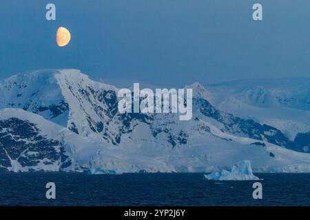 Blick auf den fast Vollmond, der über schneebedeckten Bergen auf der Antarktischen Halbinsel, Antarktis und Polarregionen aufsteigt Stockfoto