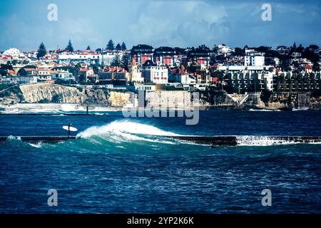 Surfer auf einem Pier mit stürmischem Meer mit Cascais Estoril Gebäuden im Hintergrund etwas außerhalb von Lissabon, Portugal, Europa Stockfoto