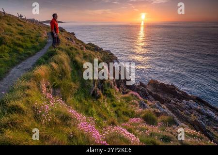 Walker mit Blick auf das Meer vom Anglesey Coast Path bei Sonnenuntergang im Frühjahr, nahe Cemaes, Anglesey, Nordwales, Vereinigtes Königreich, Europa Stockfoto