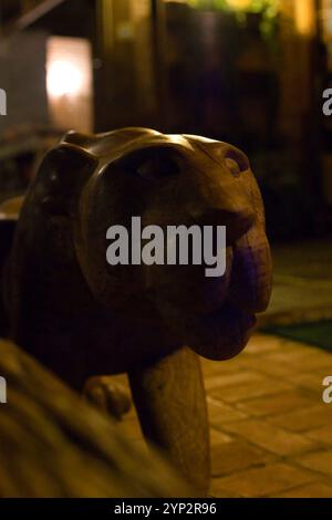 Eine hölzerne Tigerstatue steht vor einer Ziegelmauer. Die Statue ist dunkel und hat einen bedrohlichen Blick Stockfoto